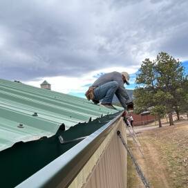 worker installing seamless gutters on a metal roof