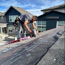 worker installing roofing underlayment on a sloped residential roof using a nailer