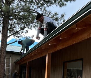 workers installing rain gutters on the edge of a Colorado home roof