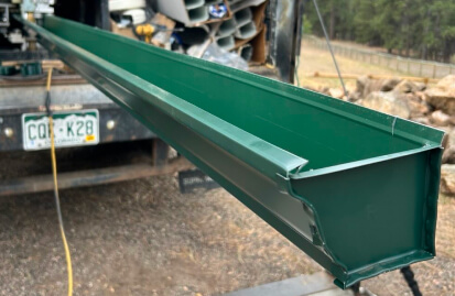 Green metal gutter section being unloaded from a work truck