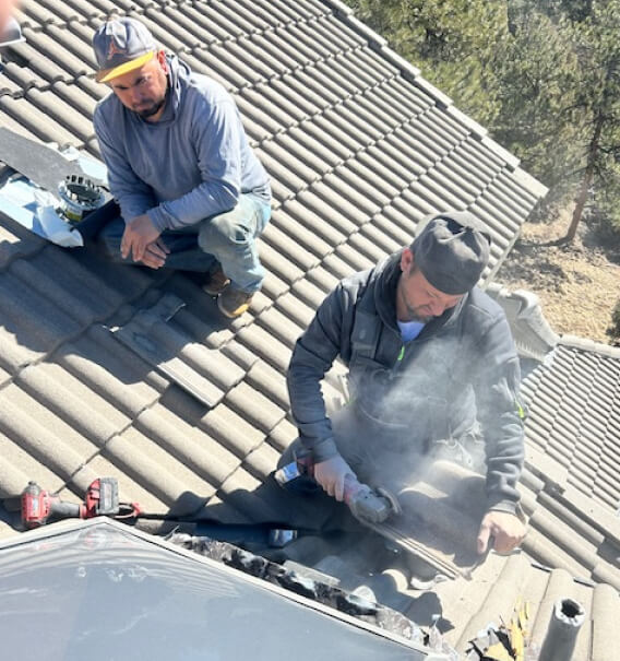 two workers repairing a damaged roof by cutting and replacing bitumen shingles