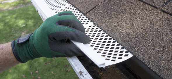 Worker installing a gutter guard on a roof edge