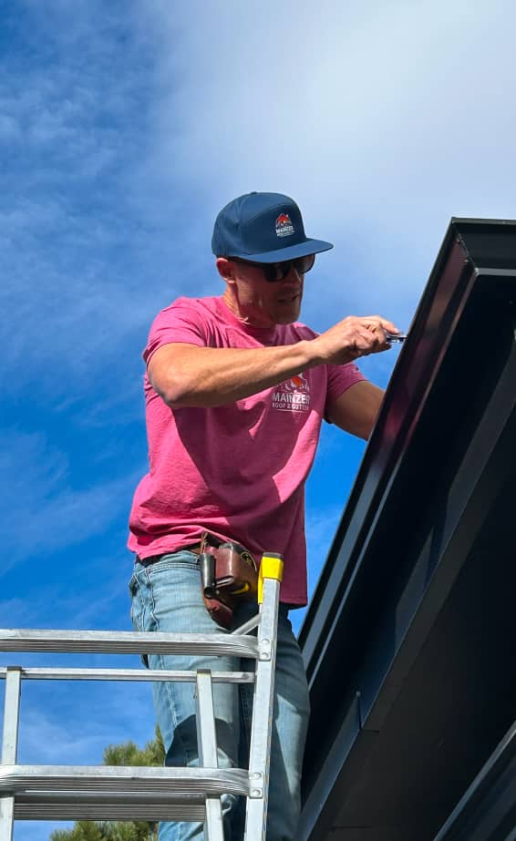 contractor installing a black metal gutter system on a roof